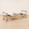 Full view of a wooden Pilates reformer with gray carriage and adjustable footbar